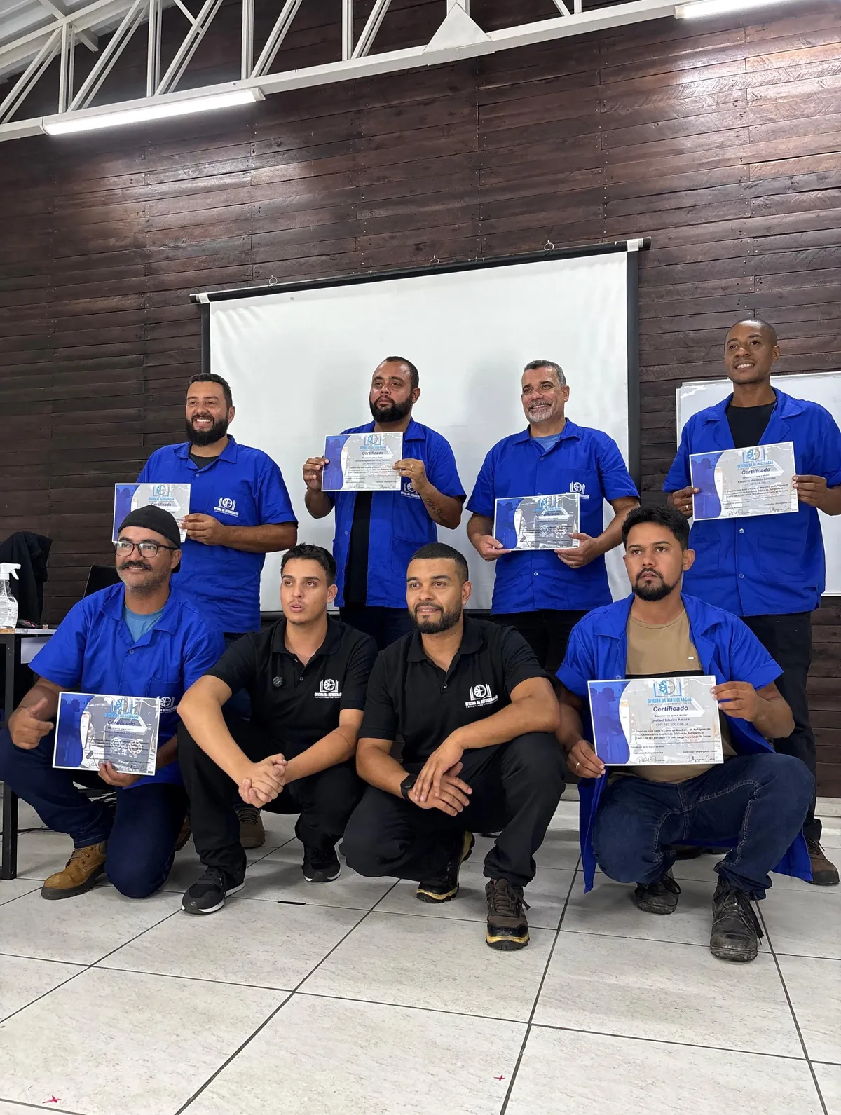 Turma de técnicos de uniforme azul segurando os certificados do curso de refrigeração comercial