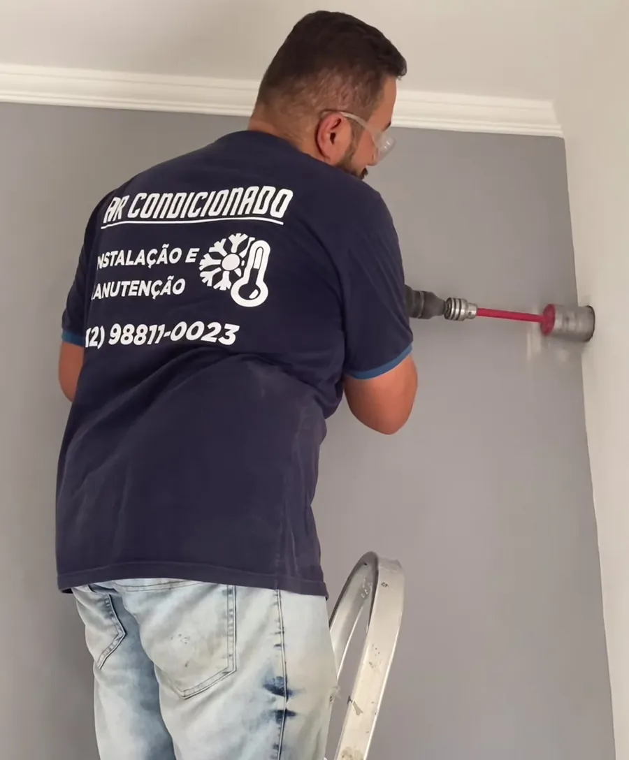 Técnico com a camiseta da Arlindo Climatização furando a parede com serra copo